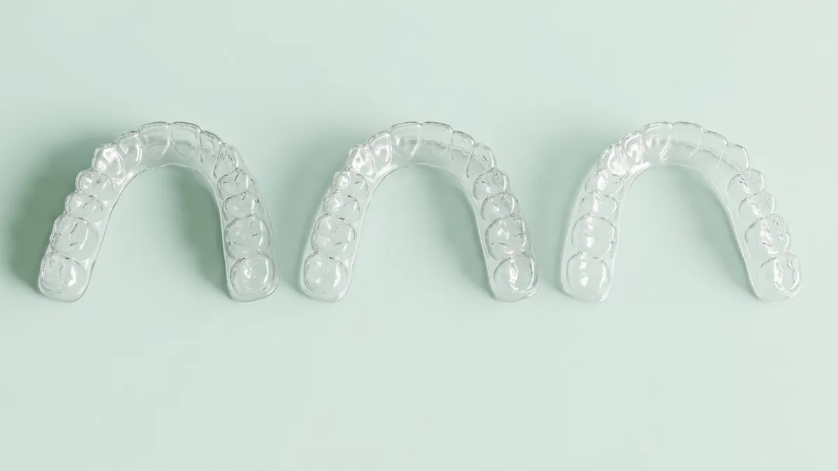 Drei transparente Aligner-Schienen liegen nebeneinander als Serie aufeinanderfolgender Behandlungsschritte