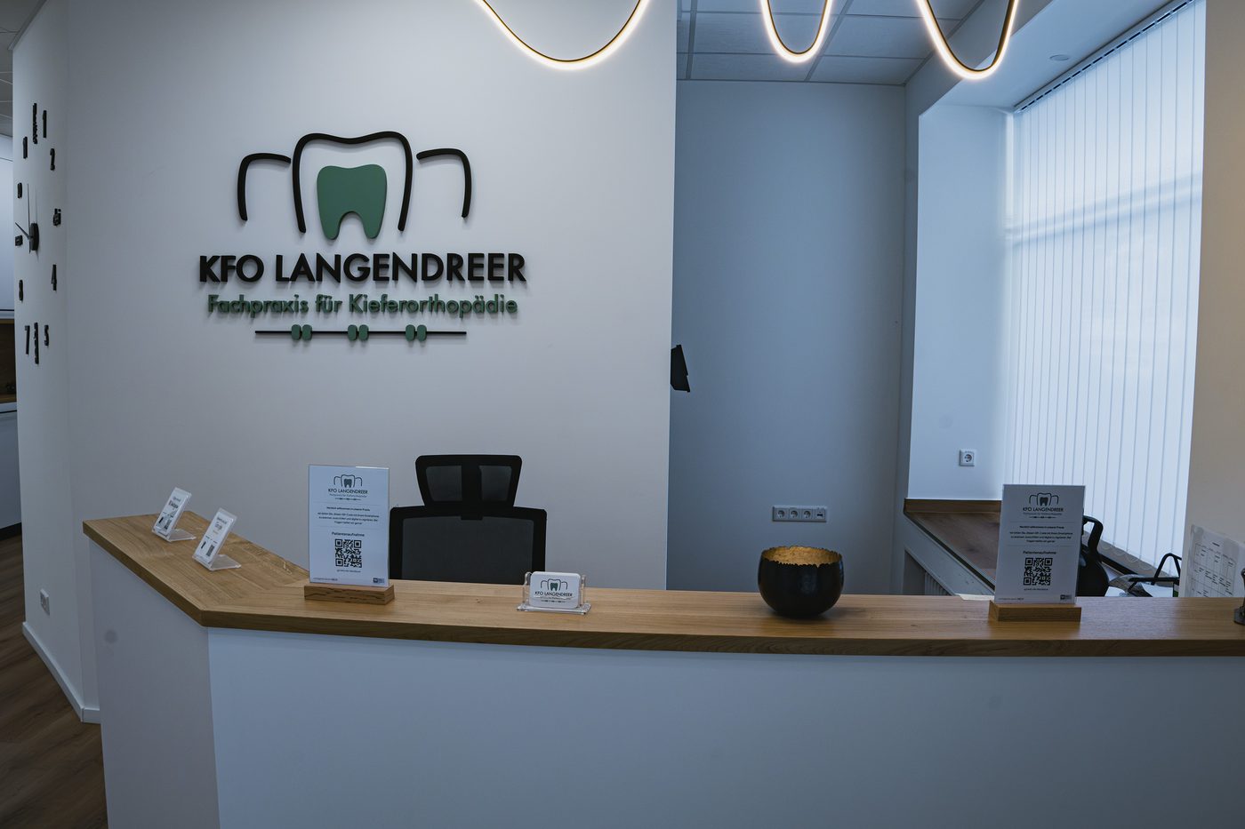 Empfangstresen der Praxis KFO Langendreer mit Wandlogo und runden Deckenleuchten
